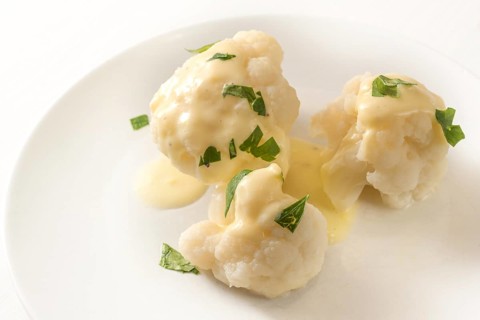Cooked cauliflower with hollandaise sauce and parsley garnish on a white plate, vegetable side