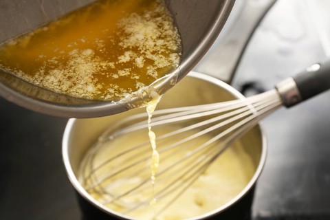 Cooking process of hollandaise sauce, pouring melted butter into the pot with egg mixture, whisking