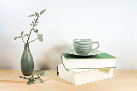 Wooden desk or table with books, a green tea cup and sage twigs in a small ceramic vase against a