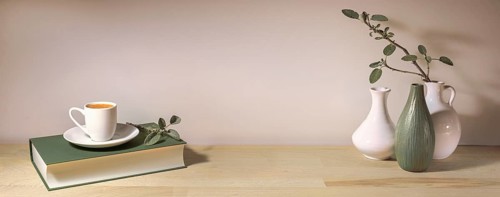 Coffee cup on a gray green book and a group of vases with a sage leaf branch on a wooden table