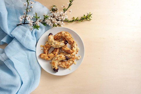 Almond crescent cookies on a plate, spring flower branch and blue napkin on a light wooden table,