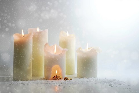 White candles burning in the snow, in one is a carve with a warm campfire, surreal winter still