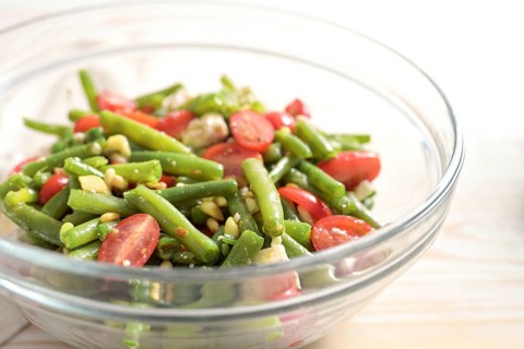 Salad of green beans, tomatoes, pine nuts and feta cheese in a glass bowl on a light wooden table,