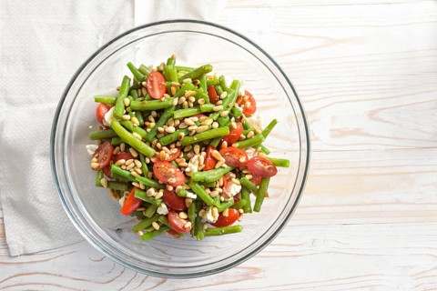 Antipasto salad of green beans, tomatoes, pine nuts and feta cheese in a glass bowl on a light