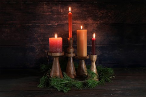 Four different candles in warm colors on wooden stands for Advent with some pine branches against a