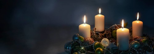 Lights in the night, four white Advent candles on a wreath with Christmas decoration against a dark