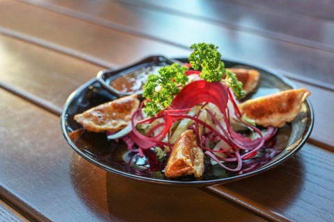 Deep fried gyoza with salad and sauce served as appetizer on a black plate, Asian dish on a wooden