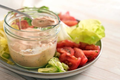 Salad dressing from skyr on a spoon and in a glass jar on a plate with slices of lettuce and