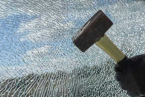 Gloved hands of a criminal destroying a laminated glass window with a hammer, violence, burglary