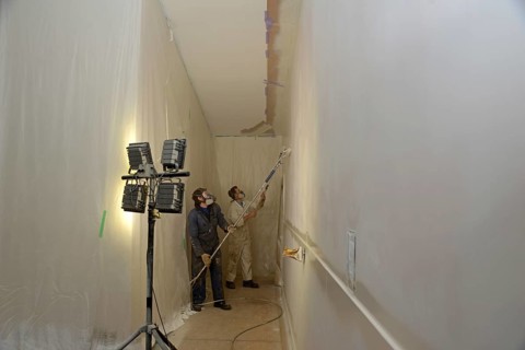 Two tradesman use airless spray equipment to paint a top coat on the walls of a commercial building