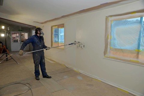 A tradesman using airless spray equipment to paint a top coat on the walls of a commercial building