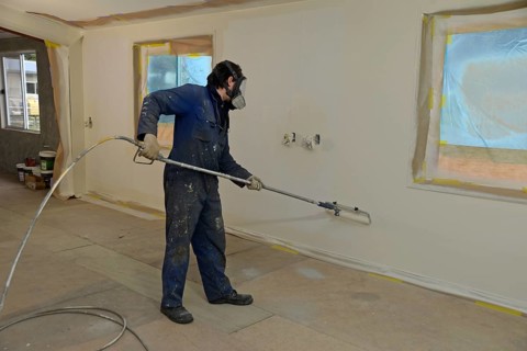 A tradesman using airless spray equipment to paint a top coat on the walls of a commercial building