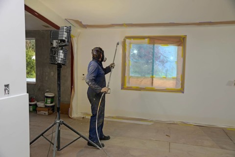 A tradesman using airless spray equipment to paint a top coat on the walls of a commercial building
