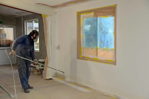 A tradesman using airless spray equipment to paint a top coat on the walls of a commercial building