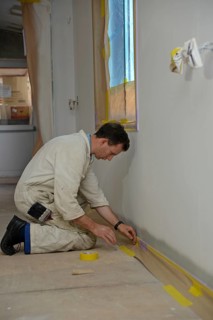 A tradesman masks off the skirting board before using airless spray equipment to paint a second