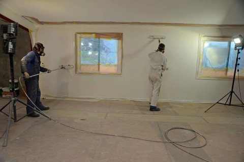 A tradesman using airless spray equipment to paint a top coat on the walls of a commercial building