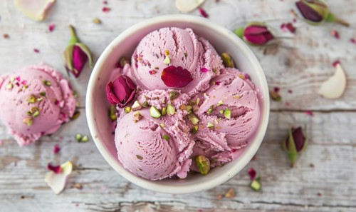 Rose petal gelato with pistachio topping on a light wooden background AI generated
