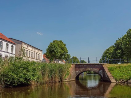 A small bridge over a river with buildings and green bushes in the background, friedrichstadt,