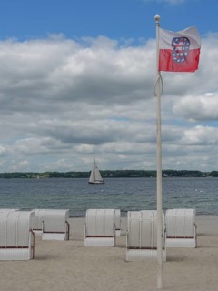 Single flag and several beach chairs on a sandy beach, sailing boat on the sea under a cloudy sky,