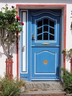 Blue decorated entrance door of a house, surrounded by blooming flowers and decorative elements,