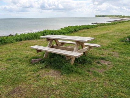 A picnic table on green grass with a view of a lake and a cloudy sky, Maasholm, Schleswig-Holstein,