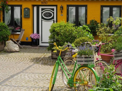 A colourful courtyard with planted bicycles, flowers and a yellow building with white window frames