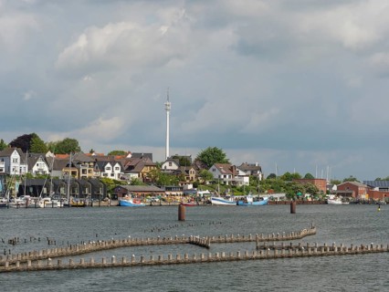 A city view with a television tower, buildings and boats on the waterfront under a partly cloudy