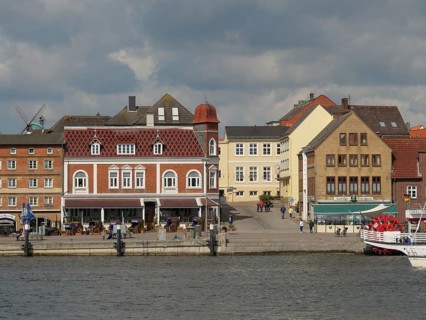 Historic buildings and tourists along a harbour shore under a cloudy sky, Kappeln,