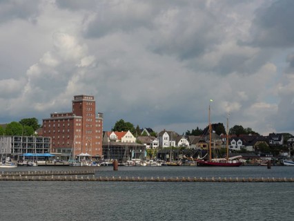 Buildings and boats along a coastline under a cloudy sky, Kappeln, Schleswig-Holstein, Germany,