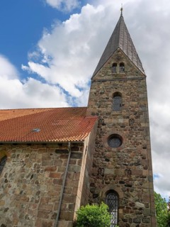 A church with a distinctive tower and red roof, under a blue sky with scattered clouds, Maasholm,