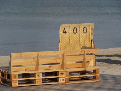 A single beach chair and a wooden bench on a quiet beach with a view of the water under a clear