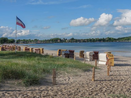 Beach with a row of beach chairs, a hedge, blue sky and clouds in the background, Eckernförde,