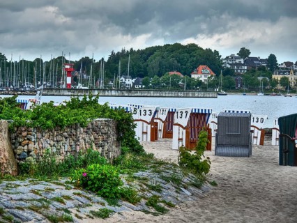 Beach with numbered beach chairs, boats in the water and a lighthouse in the background,
