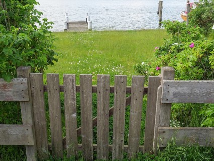 Wooden fence leading to a meadow and a body of water, surrounded by trees and flowers, Arnis,
