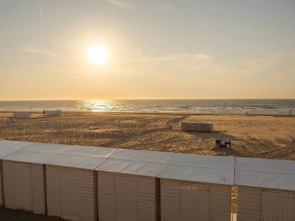 A peaceful sunset on the beach with huts in the foreground and the sea in the background, de haan,