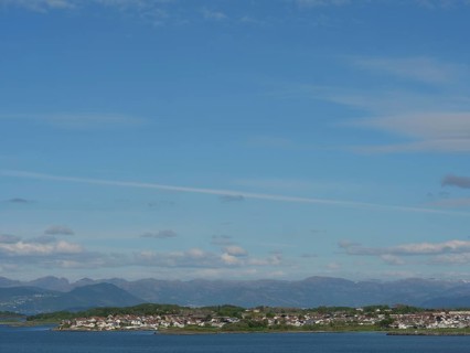 Expansive coastal landscape with a view of the sea and mountains under a slightly cloudy sky,