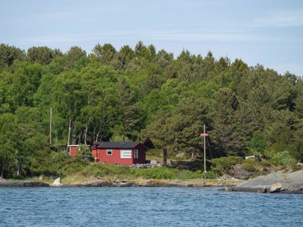 A red house on the edge of the forest near the coast, surrounded by trees and water, Stavanger,
