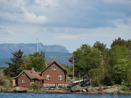 Red wooden house with flag in front of a picturesque landscape with trees, water and mountains in