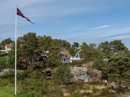 Norwegian landscape with green houses, flagstaff and wooded hills under blue sky, Stavanger,