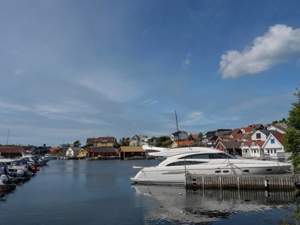 Panorama of the marina with white boats, colourful houses and calm water under a blue sky,