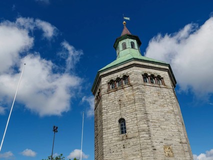 Historic stone tower with clock and flag under a bright blue sky, Stavanger, Norway, Europe