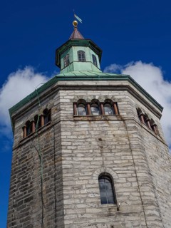 Historic stone tower with striking clock and flag. Bright blue sky in the background, Stavanger,