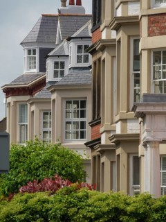 Row of townhouses with various architectural details and sloping roofs, surrounded by trees,