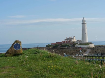 A coastal landscape with a lighthouse in the background and a stone with a plaque in the