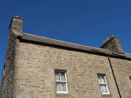 Close-up of a traditional stone house with two fireplaces under a clear blue sky, Lerwick,