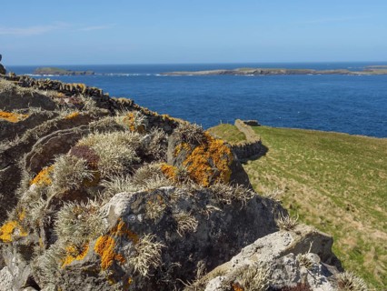 Mossy cliffs on the coast, with sweeping views of the sea and distant islands under a blue sky,