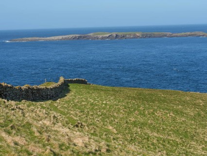 Green meadow with stone wall on the shore that merges into the wide blue sea and visible islands,