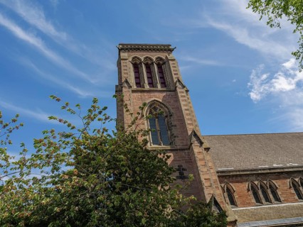 A gothic church tower rises into the sky, surrounded by trees and clouds, inverness, Scotland,