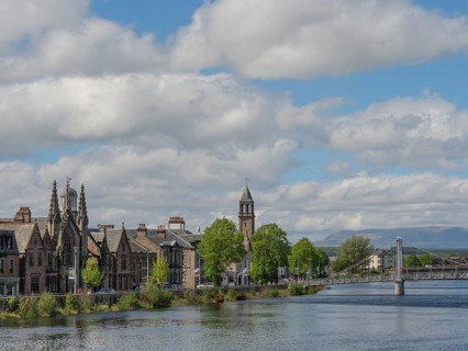 Historic buildings and a bridge over the river, surrounded by trees with mountains in the
