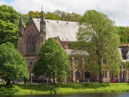 A large historic church surrounded by lush green trees, next to a tranquil river, inverness,